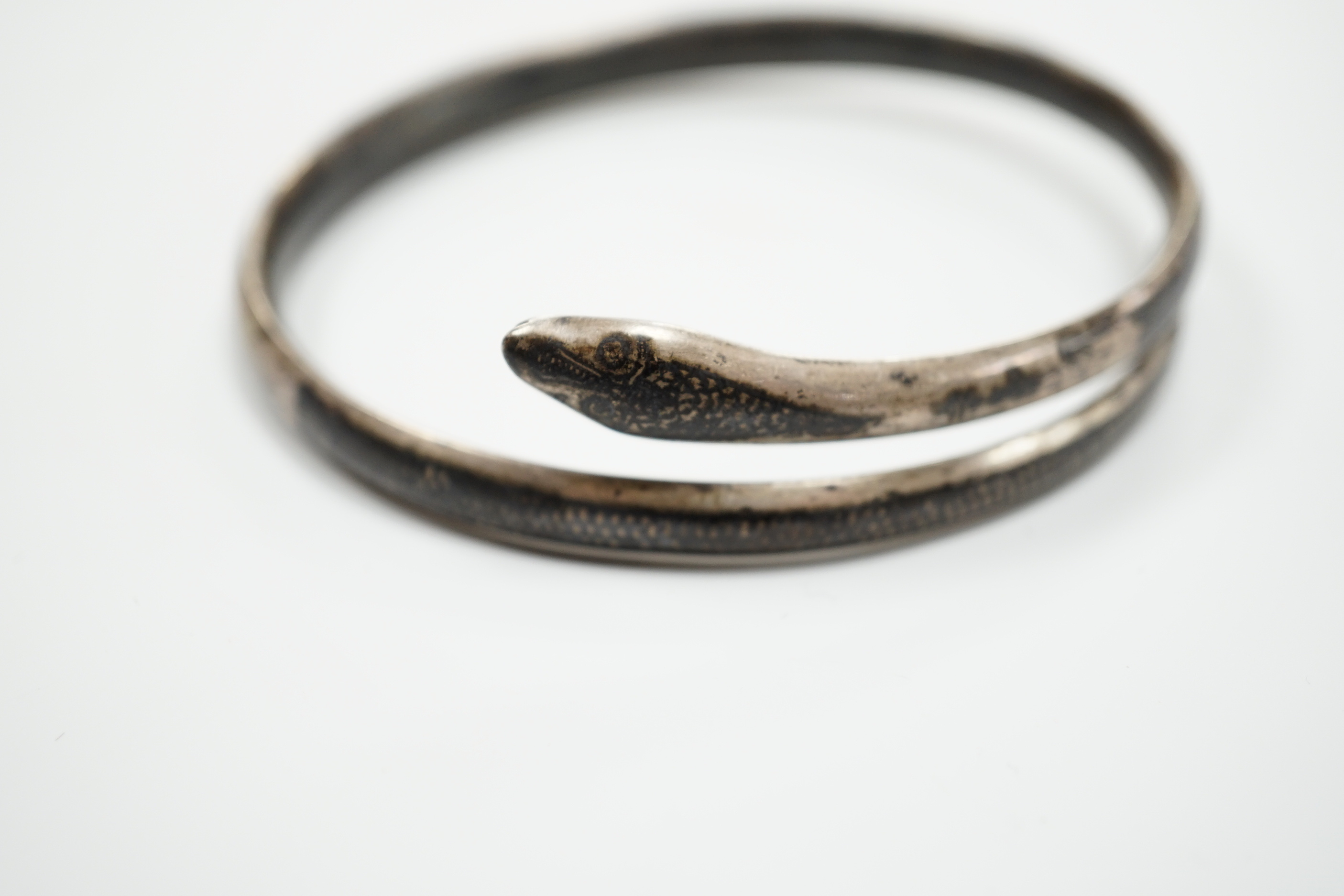 A white metal and niello serpent bangle, decorated with scene of a camel train.